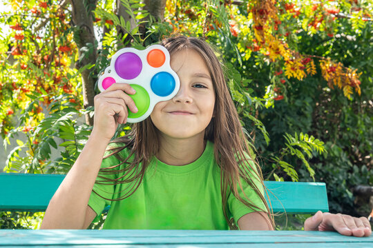 A funny girl is hiding behind a toy. Portrait little girl with a modern popit toy. Colorful and bright pop it toy simple dimple. antistress sensory toy fidget push simple dimple