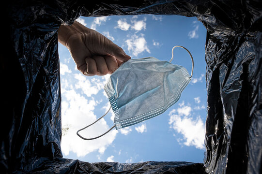 man hand throws protective medical or surgical mask into the trash outdoors. Protection against influenza and the viral ncov epidemic, quarantine, concept image.