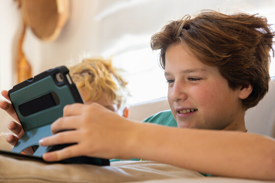 teenage boy playing video game on tablet relaxing on couch at home