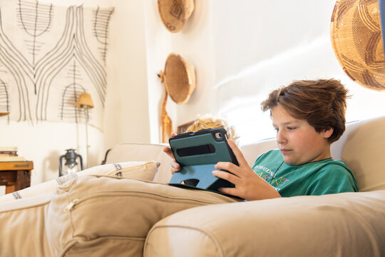 teenage boy playing video game on tablet relaxing on couch at home