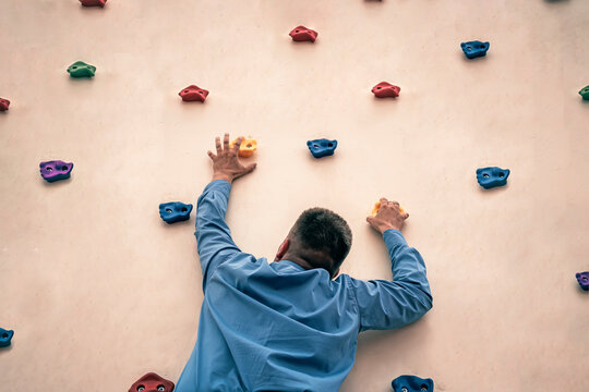 Businessman with cravat climbing a rock. Rock climbing as hobby. office worker trains in the gym. Extreme sports.