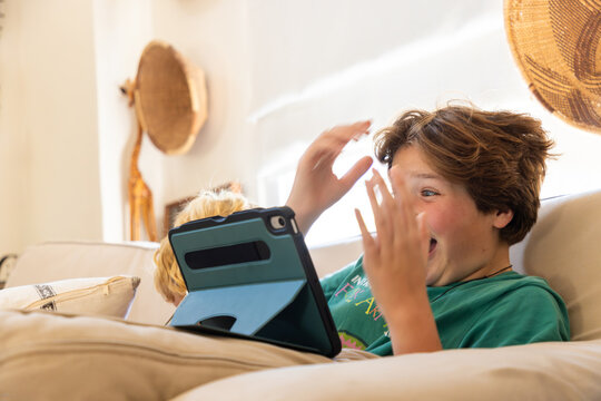 teenage boy playing video game on tablet relaxing on couch at home