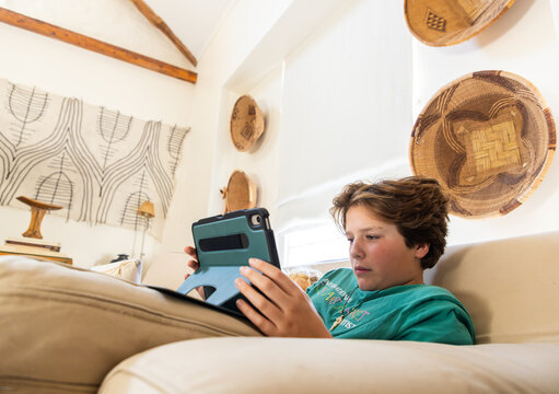 teenage boy playing video game on tablet relaxing on couch at home