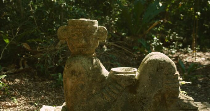 Ancient stone statue standing in dense tropical forest, illuminated by natural sunlight beneath jungle canopy in Mexico