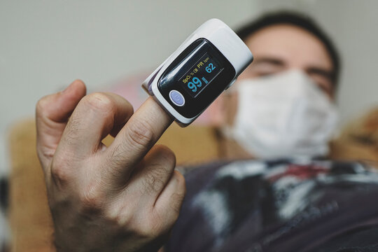 oxygen saturation of the blood. pulse oximeter on a mans finger. A patient in a medical mask measures blood saturation with an electronic pulse oximeter on his finger. high saturation of the blood.
