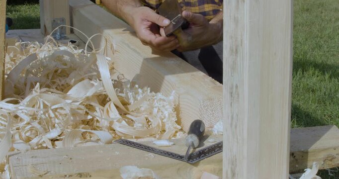 Carpenter's hands close-up. He checks the sharpness of the plane's blade with his finger and begins to plan the board. Construction and daily life in the village.