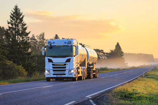 White Scania 560R milk tanker truck on a misty highway at golden hour sunrise, delivering milk to the Valio processing plant on a late summer morning. 