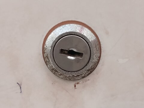 Close-Up Of A Round Metal Keyhole Lock On A White Cabinet Door