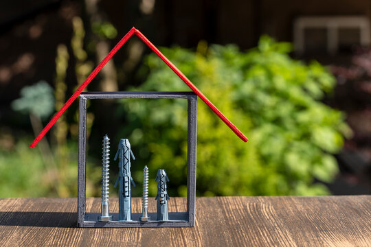 House concept made of fasteners frame and red roof. Concept of home renovation building and real estate insurance represented by screws dowels and wooden stick house model on garden background