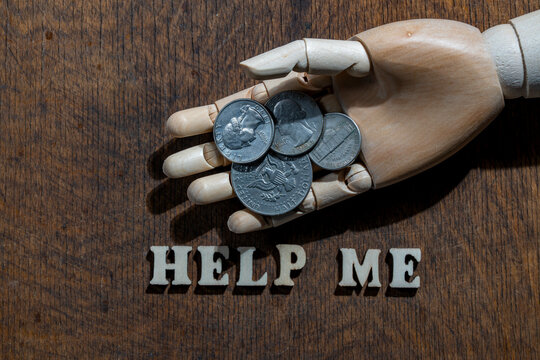 Help me concept with wooden hand and american coins. Wooden mannequin hand holding US coins above help me text letters on wood background conceptual metaphor for poverty financial crisis and charity