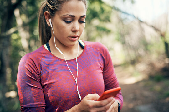 Phone, earphones and woman in nature for exercise, fitness and training with music for wellness. Park, runner and person with digital tech, audio and workout app for social media and rest in woods