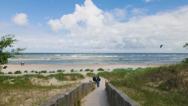 People standing on wooden path overlooking sea and dunes