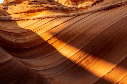 Sunlit sandstone formations with smooth, wavy layers in a desert landscape