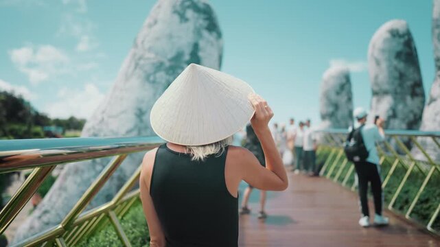 Woman walking on Golden Bridge in Vietnam, back view, slow motion. Visit Asia. Explore architectural landmark, huge stone hand holding pedestrian bridge, modern tourist location in Vietnam, excursion