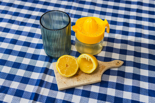 A squeezed lemon, a fruit strainer, and a glass on a kitchen table. Making homemade lemonade. Healthy lemon drink.
