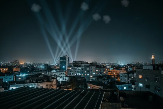 Night city skyline with bright searchlight beams illuminating the dark evening sky