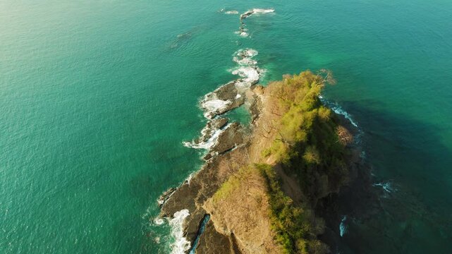 Rocky reef extends from tropical peninsula into blue Pacific Ocean water