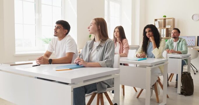 Students in classroom during lecture and discussion. Attentive group listens to a teacher, taking notes in a bright modern education space. Ideal for college learning and university study.