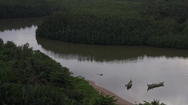 Traditional fishing canoes on winding river through lush rainforest in untouched Ghana wilderness