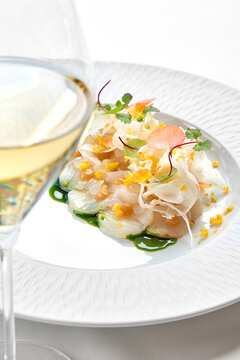 Macro shot of scallop carpaccio with green herb oil, shaved fennel, and edible flower petals on a white plate.