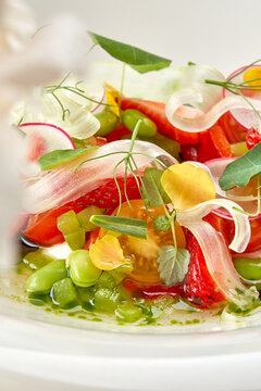Gourmet summer salad with tomatoes, strawberries, and fresh herbs in a white bowl. Fine dining restaurant dish isolated on white background
