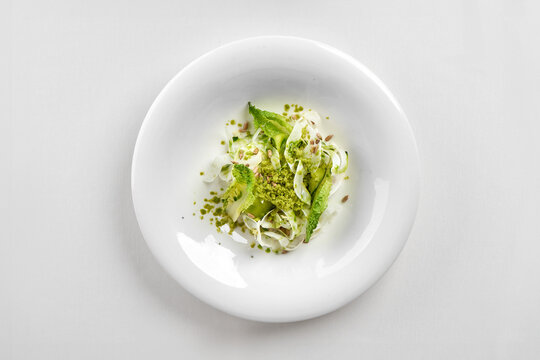 Gourmet green salad with romaine lettuce, shaved fennel, and pesto crumb in a deep white bowl. Top-down studio shot.