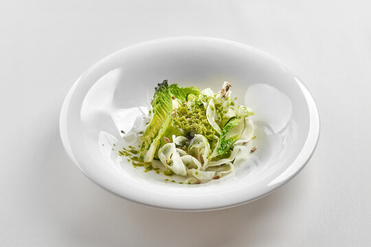 Gourmet green salad with romaine lettuce, shaved fennel, and pesto crumb in a deep white bowl. Top-down studio shot.