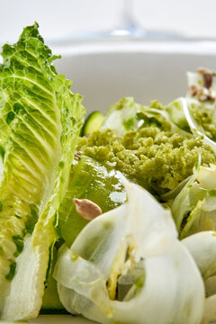 Macro shot of fresh green salad with romaine lettuce, shaved fennel, green crumb, and seeds in a white bowl.
