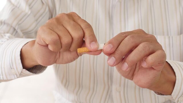 southeast asian senior man breaking a cigarette with his hands outdoors, concept of quitting smoking and choosing health, hand movement closeup shot