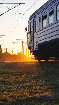 Blue train car parked on railway track at golden hour, bright sunlight silhouette of train and power lines, dramatic outdoor scene of passenger and cargo transportation vertical photo