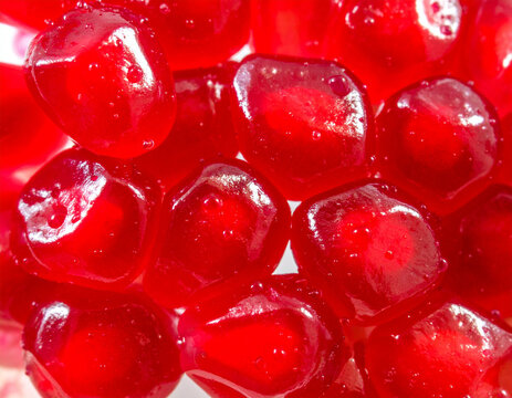 Glistening ruby red pomegranate seeds are arranged in a wet, vibrant pattern that reflects soft light for a fresh summer look.