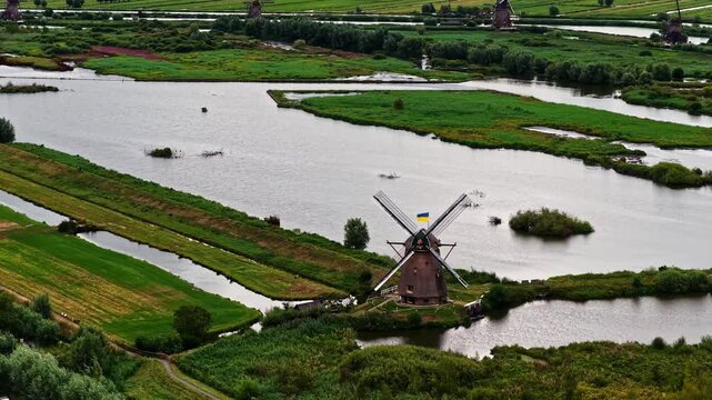A Scenic View of Historic Windmills Surrounded by Waterways, Green Fields, and Wetlands at UNESCO World Heritage Site Kinderdijk in South Holland, Netherlands - Aerial Drone Shot