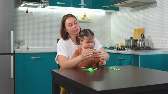 Young mother and little daughter make clay shapes together while developing fine motor skills. The educational activity reflects Montessori principles and early childhood learning. Wide shot.