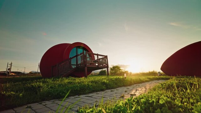 A dog trots along the paved path between terracotta qvevri shaped hotel rooms while the sun sets over the Kakheti countryside.