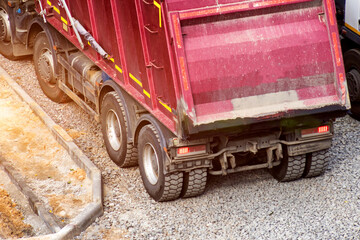 Heavy duty dump truck positioned on gravel ground at construction area, showcasing powerful wheels and illuminated rear lights, essential for road building activities. © HENADZY