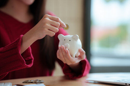 The close-up image shows a young woman planning her personal finances at home, using a piggy bank, calculator, and coins&mdash;symbols of saving, budgeting, investing, income, and future financial security.
