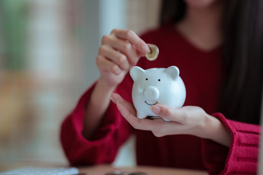 The close-up image shows a young woman planning her personal finances at home, using a piggy bank, calculator, and coins&mdash;symbols of saving, budgeting, investing, income, and future financial security.