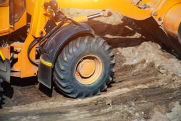 Obraz premium Heavy equipment construction loader wheel on dirt ground building site during day, showcasing robust tire hydraulic arm components industrial machinery, copy space