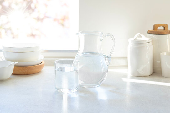 Refreshing clear pitcher and drinking glass of water on bright sunlit modern kitchen countertop