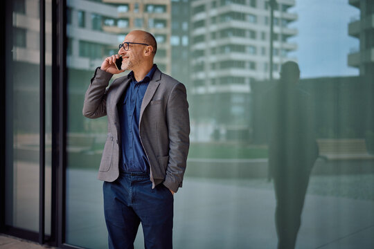 Happy businessman making phone call in front of office building.