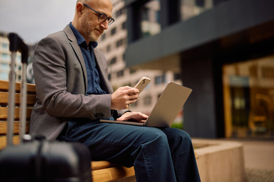 Close up of businessman using smart phone and laptop while being on work trip.
