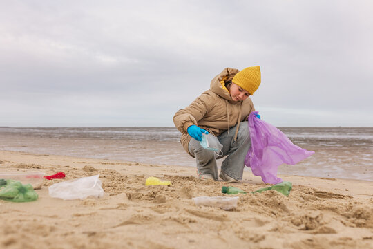 A girl collects plastic waste on the sandy beach