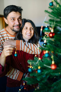 Happy husband and wife decorate a Christmas tree at home
