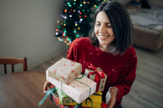 Smiling woman holds wrapped Christmas gifts at home near a tree