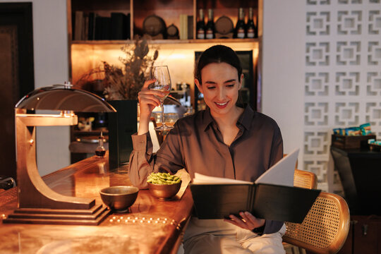 Woman reads a menu and holds a glass of wine at a hotel bar