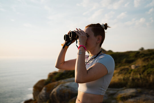 Woman observes the ocean with a binocular at sunset