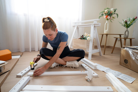 Woman assembling wooden furniture with a hammer on the floor indoors