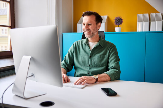 Smiling businessman works on a desktop computer in a creative office