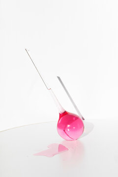 Pink liquid spills from a glass laboratory flask on a white surface