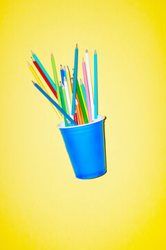 Blue plastic cup with colored pencils on a yellow background